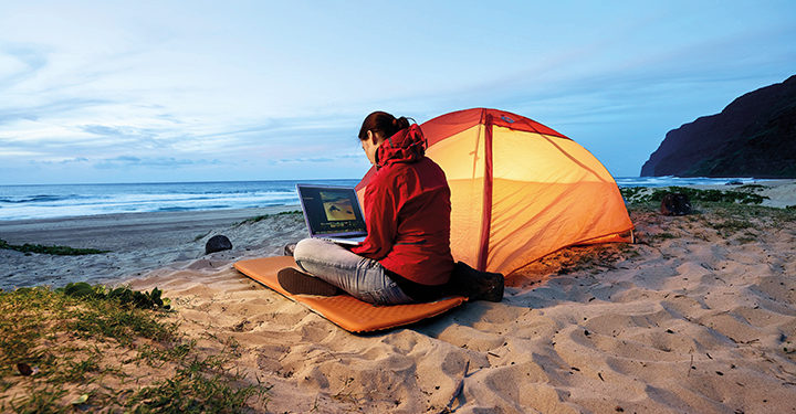 woman using laptop at tent on the beach at dusk