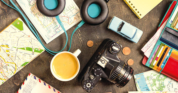 Camera, touristic maps, passport, toy car, coffee, headphones, wallet with credit cards, euro banknotes and coins on a black desk. Travel background. Tourist essentials. Plan a journey. Travel concept