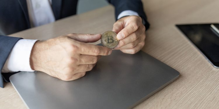 Businessman in suit holding bitcoin in his hands, sitting at desk with laptop in office interior, closeup. Successful business and savings, modern money, cryptocurrencies